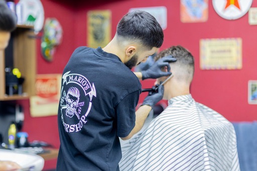 Een barbier met het Mario's-logo op zijn shirt aan het werk, van achteren gezien