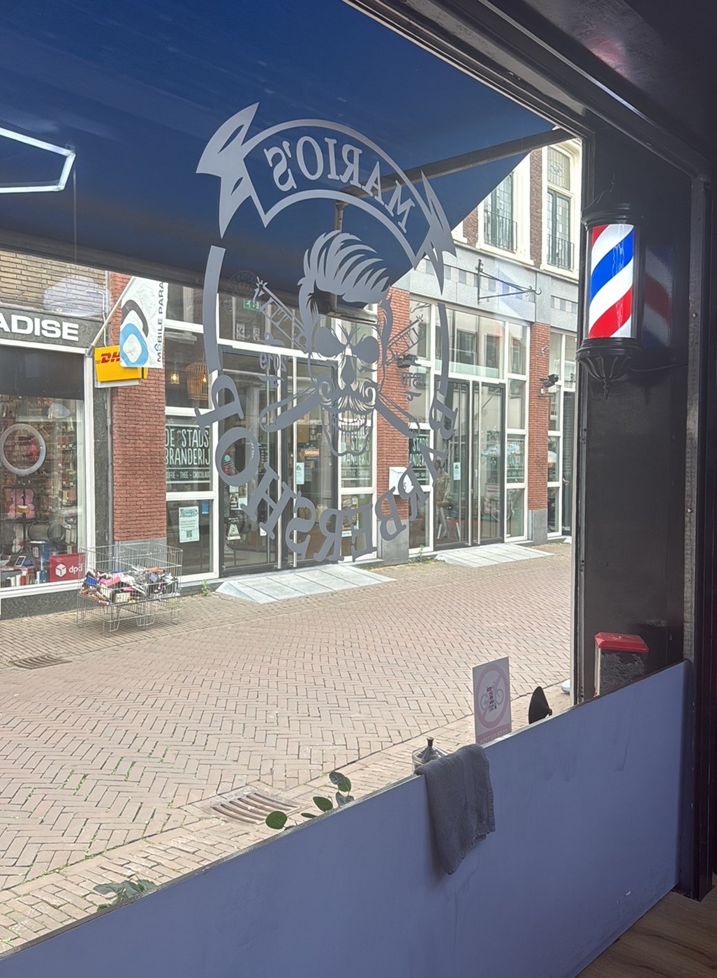 Uitzicht vanuit de zaak door de etalage met het logo en de barberpaal op de Vriesestraat